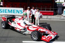 Aguri Suzuki poses next to his F1 car, surrounded by his entire workforce.